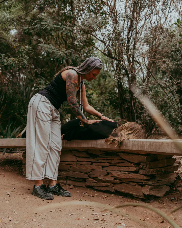 Jen leaning over a fully clothed client lying on a stone bench outdoors